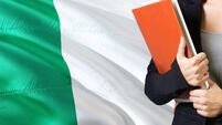 Irish Anthem curriculum.jpg Learning Irish language concept. Young woman standing with the Ireland flag in the background. Teacher holding books, orange bla