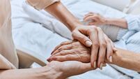 2K81GPX Relative holding trembling hand of senior woman with Parkinson's disease lying in hospital bed at medical ward. Diagnosis and tr