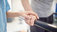 iStock-884653666.jpg Female nurse touching senior man's hand on railing
