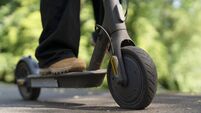 iStock-2275426628.jpg Person rides electric scooter on a path surrounded by green trees during daytime