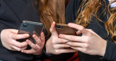 2AX9AJM teenage school girls being cyber bullies or just catching up on social media both on there phones, hand level copy space above