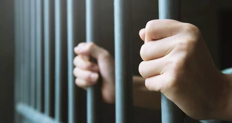 iStock-980041056.jpg Man in prison hands of behind hold Steel cage jail bars. offender criminal locked in jail.