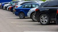 iStock-1406358314.jpg row of different color cars on asphalt parking lot at cloudy summer day