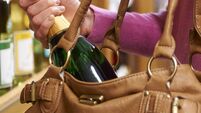iStock-186801468.jpg Woman Stealing Bottle Of Wine From Supermarket